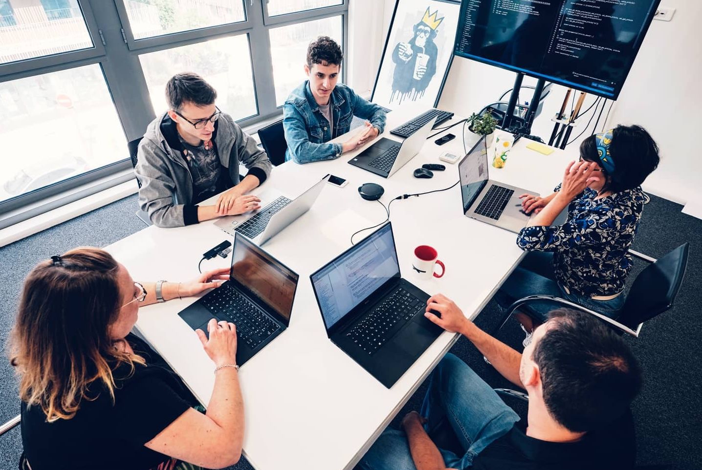 Cinq personnes en réunion dans un bureau face à un écran partagé